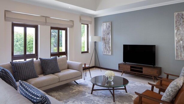 A modern living room with a sofa, coffee table, TV, and artwork on the wall. - Dubai Creek Club Villas (Dubai)