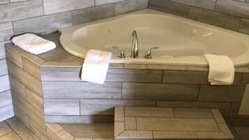 Een badkamer met een vrijstaand bad, een wastafel en een aantal houten treden die naar het bad leiden.