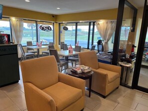 A hotel room with a dining area, two armchairs, a small table with books, and a view of the outdoors. - Unadilla/perry Near I-75 (Unadilla)
