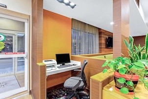 Habitación de hotel con escritorio, computadora, silla y una planta en maceta.