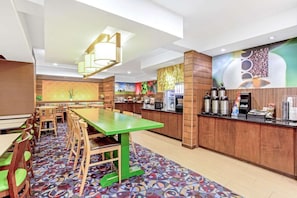 A hotel lobby with a long dining table, multiple chairs, a coffee station, and a colorful wall mural. - Manassas Hotel (Manassas)