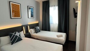 A hotel room with two beds, a headboard, a flat-screen TV, and a window with curtains. - Easyhotel Malaga City Centre (Málaga)