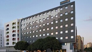 A multi-story hotel with a modern facade, a sign indicating 'Four Points Flex,' and a parking area with several cars. - Easyhotel Malaga City Centre (Málaga)