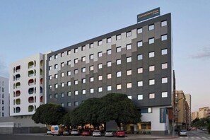 A multi-story hotel with a modern facade, a sign indicating 'Four Points Flex,' and a parking area with several cars. - Easyhotel Malaga City Centre (Málaga)