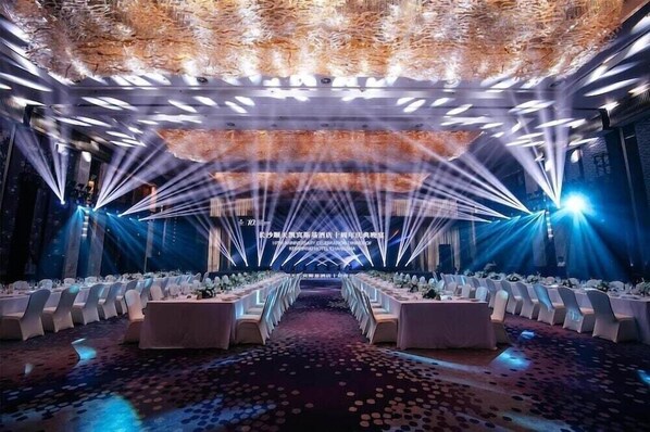 A banquet hall with rows of tables, a stage with a backdrop, and a patterned carpet. - Kempinski Hotel Changsha (Changsha)