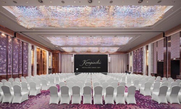 A conference room with rows of white chairs, a stage with a screen displaying 'Kempinski HOTELIERS SINCE 1897', and a ceiling with a light projection. - Kempinski Hotel Changsha (Changsha)