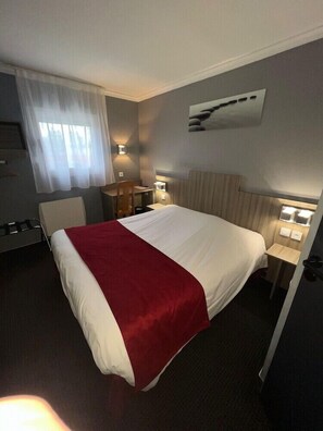 A hotel room with a bed, a desk, a chair, a lamp, and a painting on the wall. - Hotel Initial BY Balladins Amiens Longueau (Longueau)