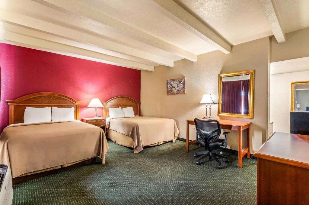 A hotel room with two beds, a desk, a chair, and a mirror.