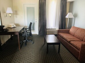 Habitación de hotel con escritorio, silla, sofá y ventana con cortinas.