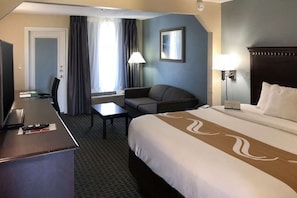 A hotel room with a bed, a desk, a chair, a television, and a window with curtains. - Quality Inn and Suites Miramar Beach (Miramar Beach)