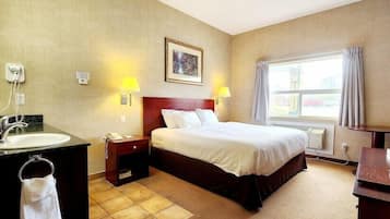 Une chambre d’hôtel comprenant un lit, une table de chevet avec une lampe, un bureau avec une chaise, une salle de bain avec un lavabo et une fenêtre avec des rideaux.