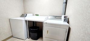 A compact laundry area with a washing machine, dryer, and a small trash bin.
