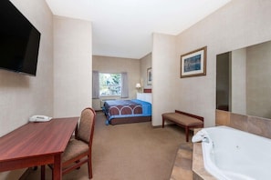 A hotel room with a bed, a desk, a chair, a TV, a bathtub, and a window.