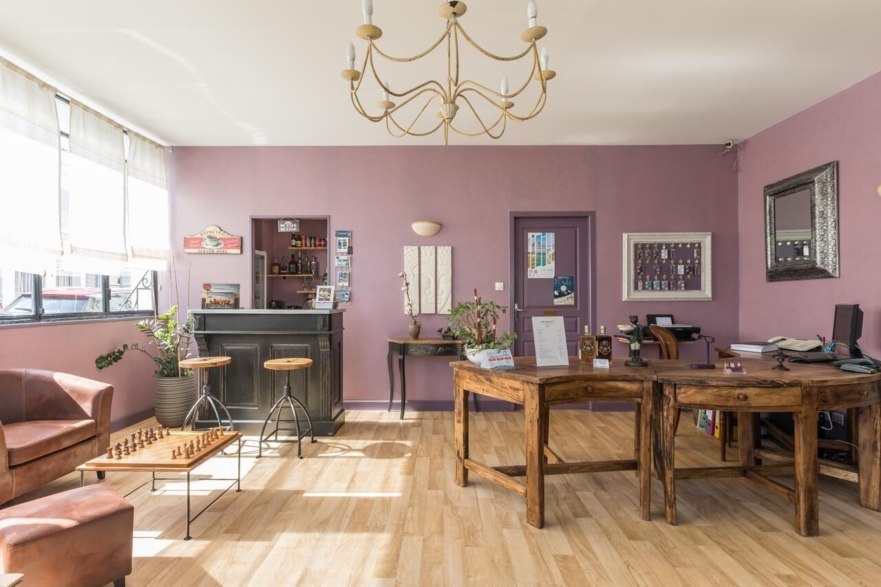 A room with a wooden floor, a chandelier, a fireplace, a chessboard, a desk, and a bar area.
