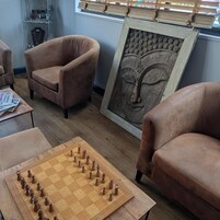 Una habitación con un tablero de ajedrez de madera, dos sillones y una obra enmarcada en la pared.