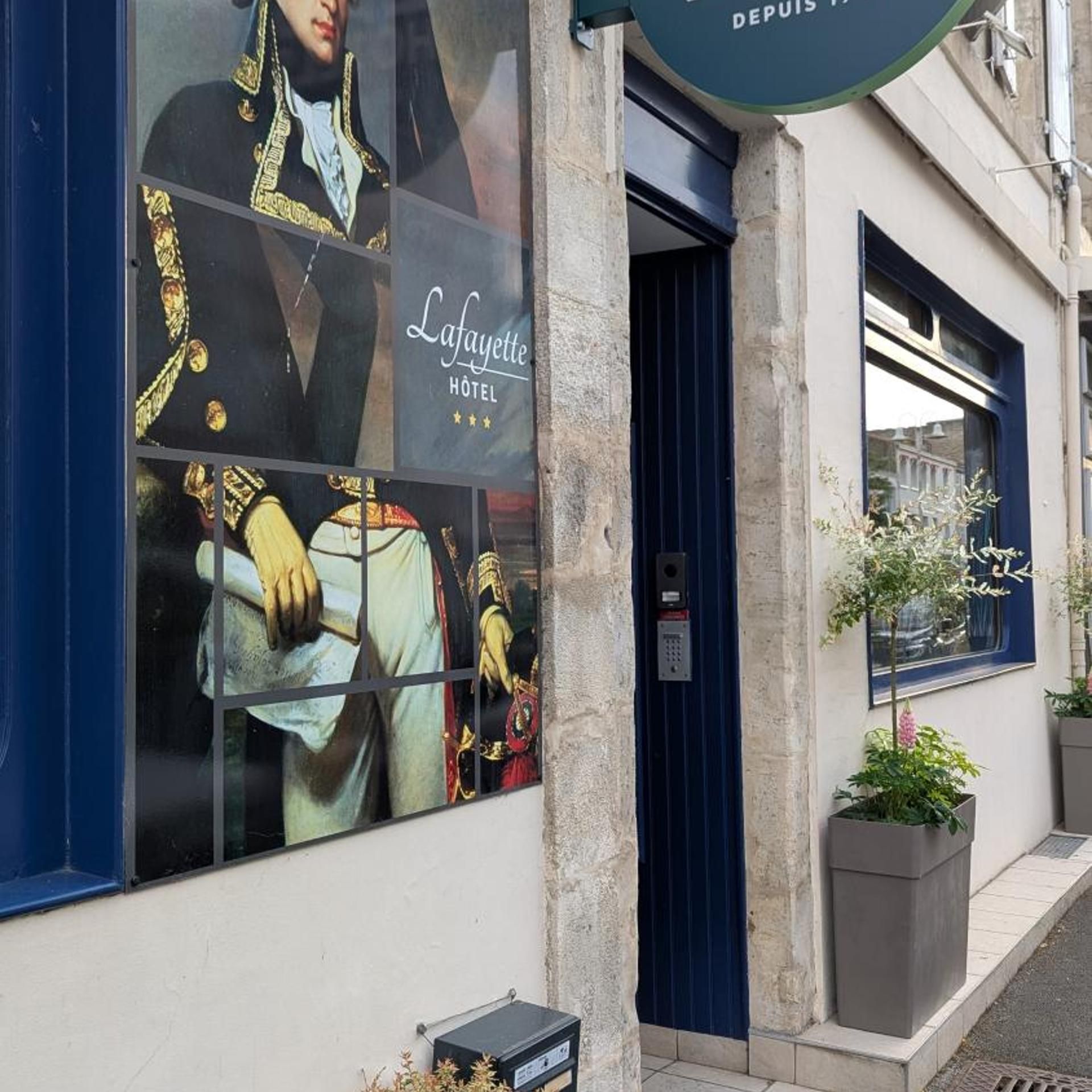 A hotel facade with a large advertisement featuring historical figures, a blue door, and a small planter with a tree.
