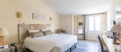 Un dormitorio amplio con una cama grande, un escritorio y una silla. Hay una maleta en el suelo y una lámpara sobre el escritorio.
