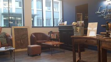 Un hall d’hôtel avec une table d’échecs, un canapé et une grande fenêtre donnant sur le bâtiment.