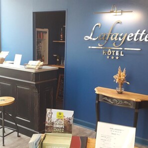 Mostrador de recepción de hotel con un cartel que dice 'Lafayette Hotel' y un expositor de guías turísticas.