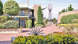 A hotel entrance with a clear pathway leading to the building, surrounded by well-maintained greenery and a distinctive tower structure.