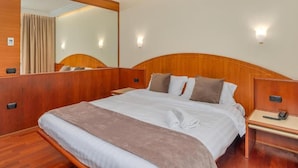 A hotel room with a large bed, wooden headboard, bedside tables, and a mirror.