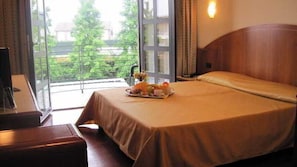 Habitación de hotel con cama, una mesa con una bandeja de frutas, un escritorio y vistas a zonas verdes a través de la ventana.