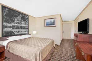 Ein Hotelzimmer mit einem Bett, einem Fernseher, einem Gemälde und einem gemusterten Teppich.