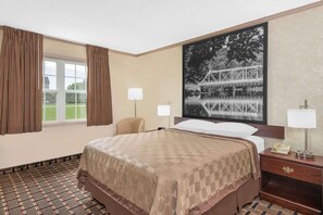 Ein Hotelzimmer mit einem großen Bett, einem Schreibtisch mit Telefon, zwei Nachttischlampen, einem Fenster mit Vorhängen und einem großen gerahmten Bild an der Wand.