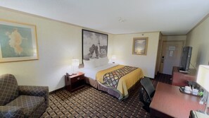 Ein Hotelzimmer mit einem Bett, einem Schreibtisch mit Computer, einem Sessel, einem kleinen Tisch und einem Fernseher.