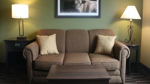 A room with a brown sofa, two side tables with lamps, a framed picture of a bull, and a patterned floor. - Yonder Inn (Beeville)