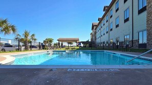 A swimming pool with a no diving sign, surrounded by a fence, palm trees, and a building with multiple windows. - Comfort Inn & Suites Beeville, TX (Beeville)