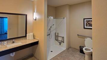 A bathroom with a sink, mirror, shower, toilet, and a framed picture on the wall.