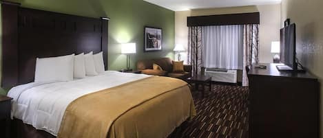 A hotel room with a large bed, a desk, a chair, a television, and a window with curtains.