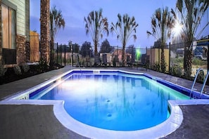 Una piscina de borde curvo, rodeada por una valla y palmeras.