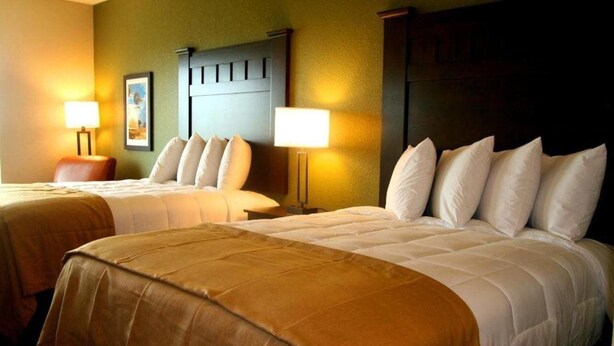 A hotel room with two beds, each with a headboard, bedside lamps, and a framed picture on the wall. - Yonder Inn (Beeville)