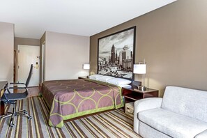 A hotel room with a bed, a desk with a chair, a sofa, and a large cityscape painting on the wall. - Delavan Inn and Suites (Delavan)
