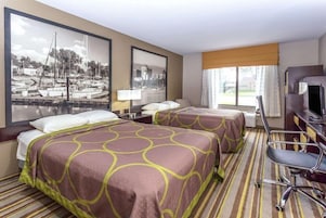 A hotel room with two beds, a desk, a chair, and a television.