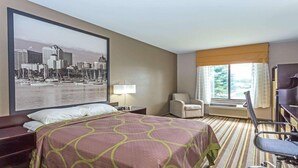 A hotel room with a large bed, a desk, a chair, a lamp, and a window with curtains. - Delavan Inn and Suites (Delavan)