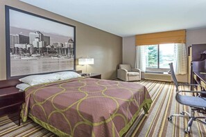 A hotel room with a large bed, a desk, a chair, a lamp, and a window with curtains. - Delavan Inn and Suites (Delavan)
