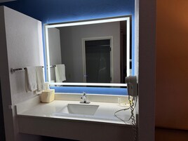 A bathroom with a white sink, a mirror with built-in lighting, and a towel rack.