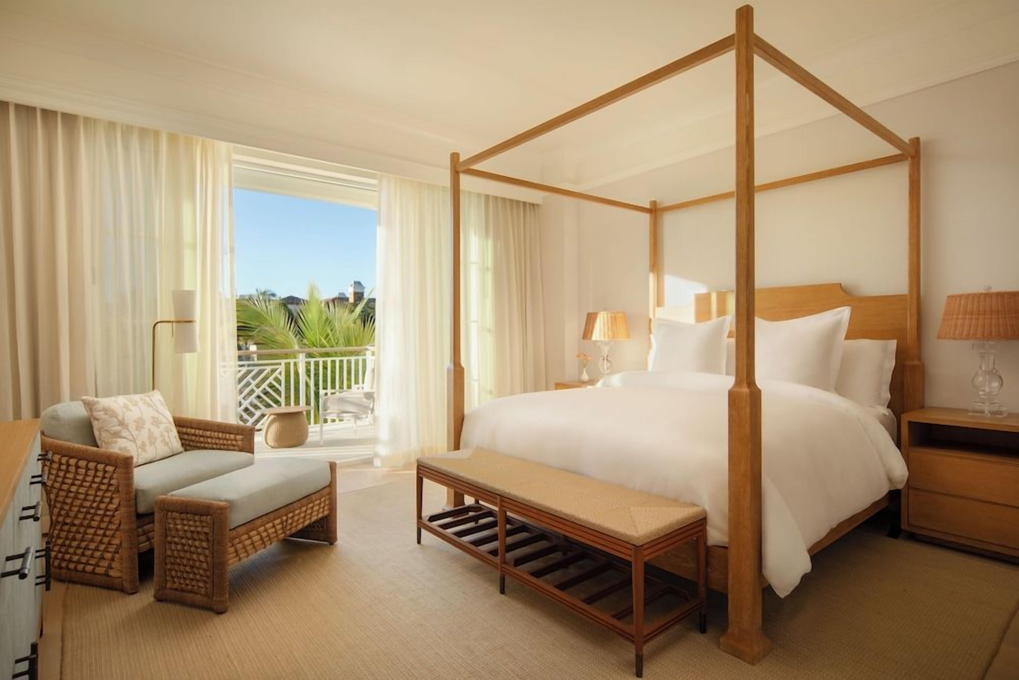 A four-poster bed with a wooden frame, a chaise lounge, a small bench, and a nightstand with a lamp.