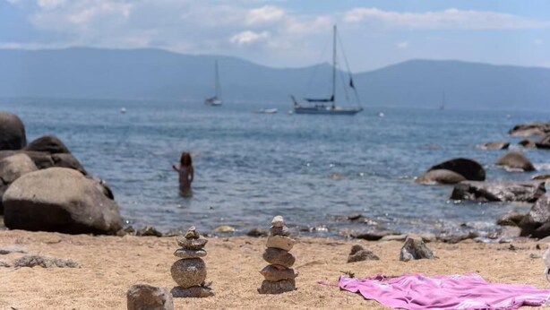 A beach with stacked stones, a pink cloth, and boats in the water. - Hotel Le Golfe (Serra-di-Ferro)
