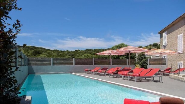 A swimming pool with red lounge chairs and umbrellas, surrounded by a stone building and greenery. - Le Golfe, Piscine & Spa Casanera (Serra-di-Ferro)