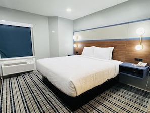 A hotel room with a bed, bedside tables, a lamp, a heater, and a window with a blind. - Americinn by Wyndham Rawlins (Rawlins)