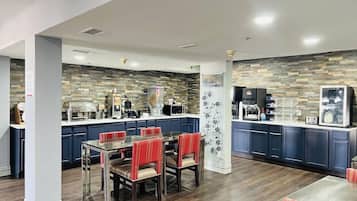 A modern kitchen with a stone backsplash, a dining area with red upholstered chairs, and a coffee station.