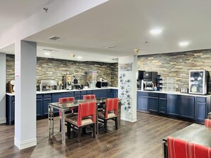 Een moderne keuken met een backsplash van steen, een eethoek met rode beklede stoelen, en een koffiehoek.