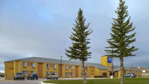A hotel with a yellow facade, multiple windows, and a parking lot with several cars. - Americinn by Wyndham Rawlins (Rawlins)