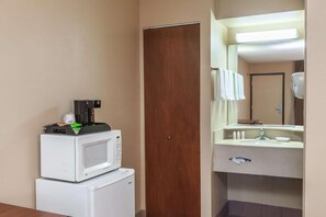A hotel room with a microwave on a small refrigerator, a wooden door, and a bathroom with a sink and mirror. - Red Carpet Inn Elkton (Elkton)