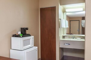 A hotel room with a microwave on a small refrigerator, a wooden door, and a bathroom with a sink and mirror.