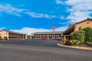 A motel with a central building and two wings, a red sign, and a parking lot.